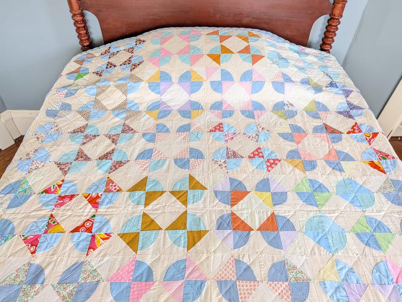 Puede incluir: Un edred&oacute;n hecho a mano con un patr&oacute;n repetitivo de formas coloridas en tonos de azul, rosa, naranja y amarillo. El edred&oacute;n est&aacute; colocado sobre una cama con un cabecero de madera. El dise&ntilde;o incluye semic&iacute;rculos y tri&aacute;ngulos.