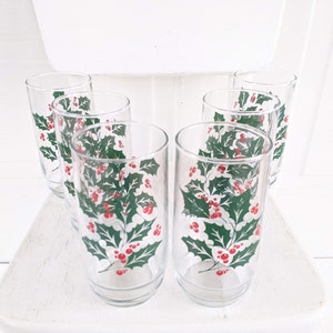 May include: Set of six clear glass drinking glasses with a holly and berry design. The glasses have a white background with green holly leaves and red berries.