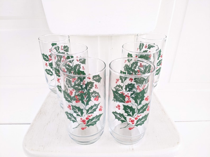 May include: Set of six clear glass drinking glasses with a holly and berry design. The glasses have a white background with green holly leaves and red berries.