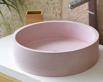 Könnte beinhalten: Ein rundes, pinkfarbenes Waschbecken aus Beton mit einer glatten, matten Oberfläche.
