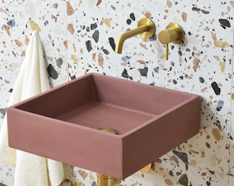 May include: A dusty rose colored rectangular bathroom sink with a gold faucet and a gold knob on a tiled wall with brown, white, and black flecks.