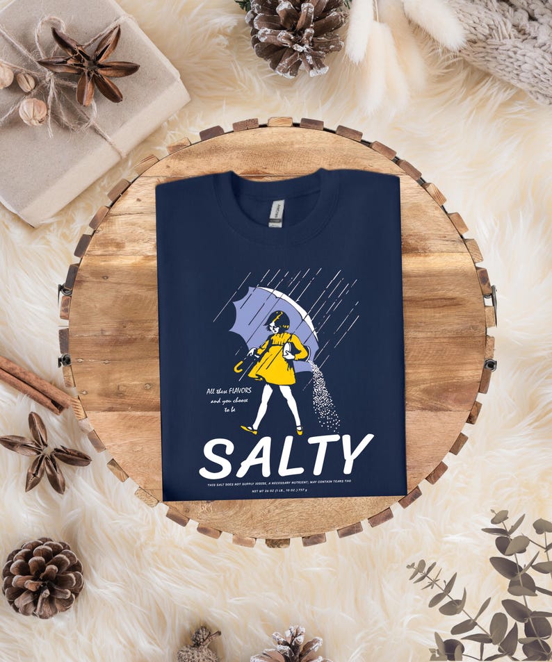 Puede incluir: Camiseta azul marino con un gr&aacute;fico de una persona bajo un paraguas, con la palabra "SALTY" en blanco. El gr&aacute;fico incluye el texto "All these flavors and you choose to be".