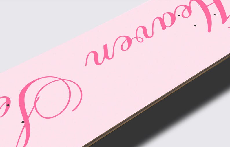 May include: A light pink skateboard deck with the cursive text "So Heaven" in a darker pink. The deck has a wooden edge and is set against a light gray background.