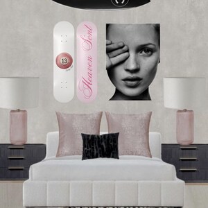 May include: A bedroom scene featuring a black surfboard with a white logo, two skateboards, a black and white portrait, a bed with pillows, and two lamps. One skateboard is white with a pink 13 ball, the other is pink with the text "Heaven Sent".