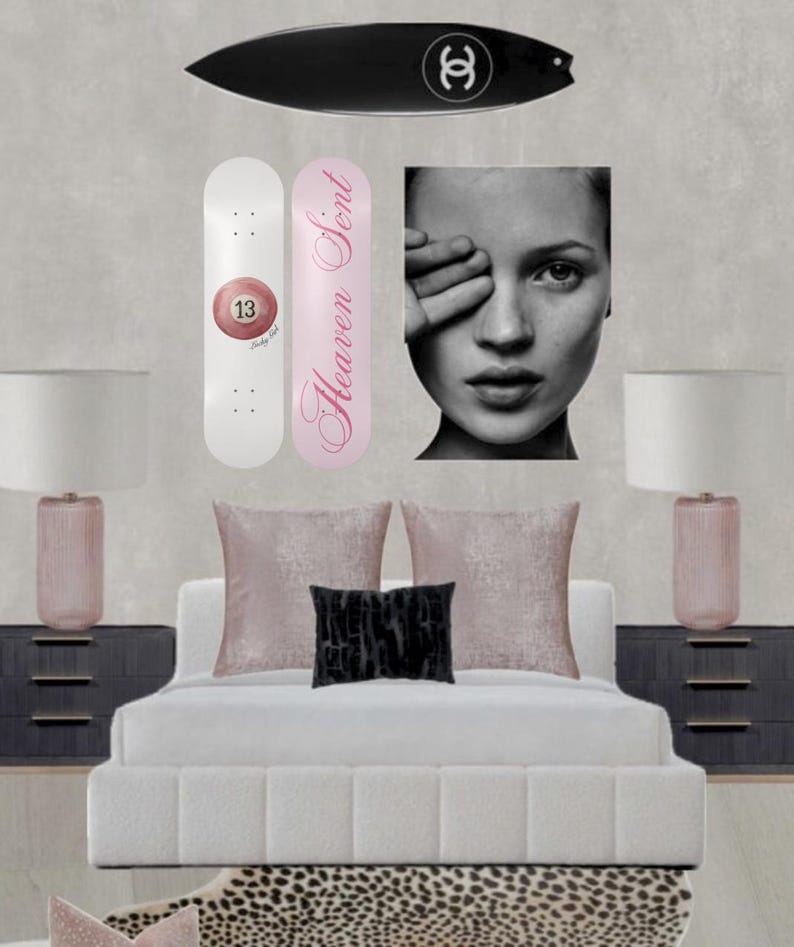 May include: A bedroom scene featuring a black surfboard with a white logo, two skateboards, a black and white portrait, a bed with pillows, and two lamps. One skateboard is white with a pink 13 ball, the other is pink with the text "Heaven Sent".