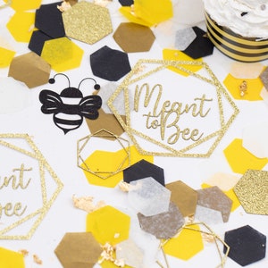 May include: Gold glitter confetti with a bee and geometric shapes with the text "Meant to Bee" on a white background.