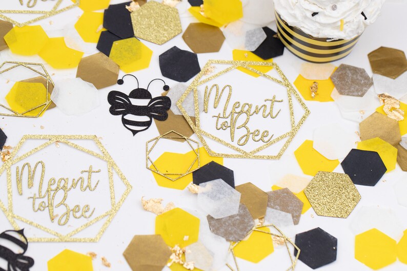 May include: Gold glitter confetti with a bee and geometric shapes with the text "Meant to Bee" on a white background.