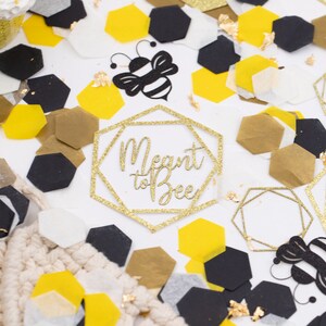 May include: Gold glitter geometric shapes with the text "Meant to Bee" and black and yellow bee cutouts on a white background with gold, black, and white confetti.