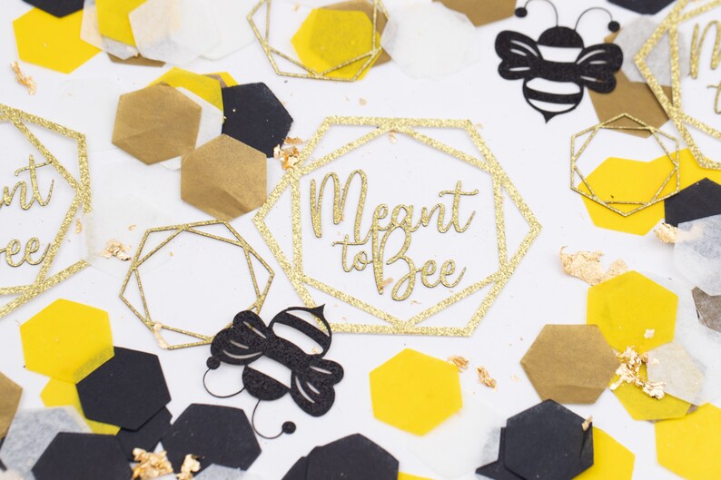 May include: Gold glitter confetti with black and yellow honeycomb shapes, a black bee cutout, and a gold glitter geometric frame with the text "Meant to Bee".