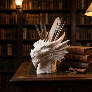 Op de afbeelding: Een witte drakenhoofdsculptuur, gebruikt als pen- en penseelhouder, met veren en kunstbenodigdheden erin. De sculptuur staat op een houten bureau in een bibliotheek, met boeken op de achtergrond.