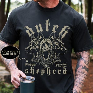 May include: Black t-shirt featuring a graphic of three German Shepherd dog heads with the text "Autck shepherd". The design includes the name "Freya" and the phrase "Not a Pet. A Partner."