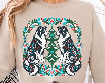 May include: A beige crewneck sweatshirt featuring a graphic print of two black and white dogs facing a central green pine tree. The design is framed by a wreath of green leaves, red berries, blue snowflakes, and geometric floral patterns.