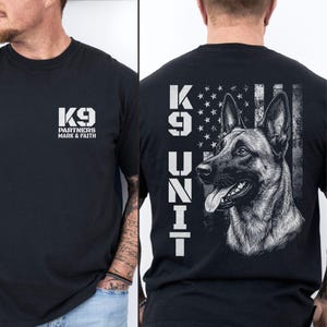 May include: A black t-shirt featuring a white graphic on the front chest that reads K9 PARTNERS MARK & FAITH. The back displays a large white graphic of a German Shepherd, the text K9 UNIT, and a stylized American flag background design.