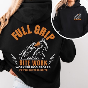 Puede incluir: Una sudadera negra con capucha que presenta un gráfico en la espalda de un perro mordiendo una manga protectora, con el texto FULL GRIP BITE WORK WORKING DOG SPORTS POWER CONTROL DRIVE. El pecho delantero tiene un gráfico más pequeño.