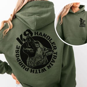 May include: An olive green hoodie featuring a black graphic of a dog's head and the text "K9 Handler Train With Purpose." The front of the hoodie has a small graphic of a dog and the words "K9 Loki."