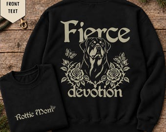 May include: A black sweatshirt featuring a graphic of a Rottweiler dog surrounded by roses and butterflies with the text Fierce devotion. A smaller black sweatshirt is shown with the text Rottie Mom and a butterfly graphic.