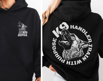 May include: A black hooded sweatshirt featuring a white graphic of a German Shepherd on the front left chest with the text K9 ALPHA. The back displays a large circular graphic of a German Shepherd with the text K9 HANDLER TRAIN WITH PURPOSE.