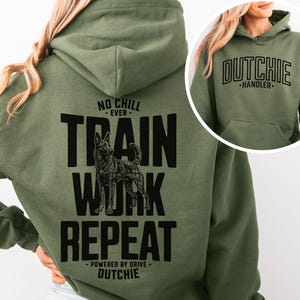 Puede incluir: Una sudadera con capucha verde oliva que presenta un gráfico negro en la espalda con la ilustración de un perro y el texto NO CHILL EVER TRAIN WORK REPEAT POWERED BY DRIVE DUTCHIE. El pecho muestra el texto DUTCHIE HANDLER en negro.