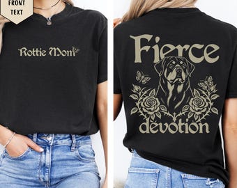 May include: A black short-sleeve t-shirt featuring the text "Rottie Mom" on the front. The back displays a Rottweiler dog illustration surrounded by roses, butterflies, and the text "Fierce devotion" in a light beige color.