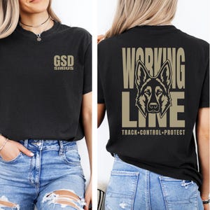 May include: A black t-shirt featuring a small tan graphic on the front chest that reads GSD SIRIUS. The back of the shirt displays a large tan graphic of a German Shepherd dog head centered between the words WORKING LINE with TRACK CONTROL PROTECT.
