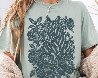 May include: A sage green short-sleeve t-shirt featuring a dark charcoal graphic print of a Cane Corso dog surrounded by detailed floral illustrations of blooming peonies and leaves centered on the front of the garment.