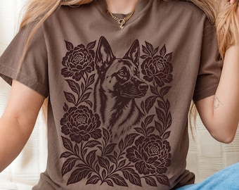May include: A brown short-sleeved t-shirt featuring a dark brown graphic print of a German Shepherd dog head surrounded by detailed floral illustrations of blooming flowers and leaves centered on the front of the garment.