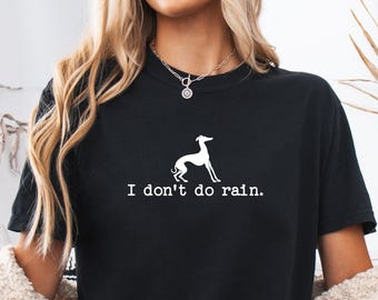 May include: A black short-sleeved t-shirt featuring a white graphic of a greyhound dog standing in profile. Below the dog, the text "I don't do rain." is printed in a white, clean, sans-serif font. The shirt has a classic crew neckline.