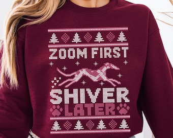 May include: A maroon crewneck sweatshirt featuring a white and light pink knit-style graphic. The design includes rows of pine trees and hearts, a running greyhound silhouette, and the text "ZOOM FIRST SHIVER LATER" with paw prints.