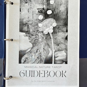 Könnte beinhalten: Ein schwarz-weißes Handbuch für das Magical Nature Tarot Deck. Das Cover zeigt ein stilisiertes Bild einer Person, die eine Blume hält, um die herum Blasen schweben. Der Text "GUIDEBOOK" ist in großen, fetten Buchstaben mit dem Text "MAGICAL NATURE TAROT" darüber und "by the SINK Spirit Collective" darunter.