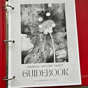 May include: A black and white image of a guidebook for the Magical Nature Tarot deck. The cover features a stylized image of a flower with a person blowing bubbles.