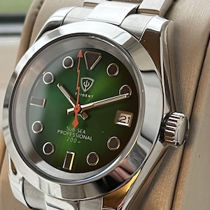 Puede incluir: Un reloj de pulsera de acero inoxidable con esfera verde. El reloj tiene una visualización de fecha a las 3 en punto y el texto "SUB SEA PROFESSIONAL 200 m". Tiene una correa plateada y una corona en el lado derecho.