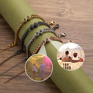 May include: A collection of personalized bracelets in gold, black, silver, and copper tones. Each bracelet features a chain design and a round pendant with a photo. The bracelets are displayed on a green surface.