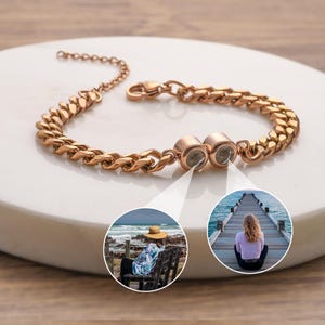 May include: Rose gold bracelet with a curb chain design. The bracelet features a lobster clasp closure and two round, decorative elements. The bracelet is displayed on a white surface.