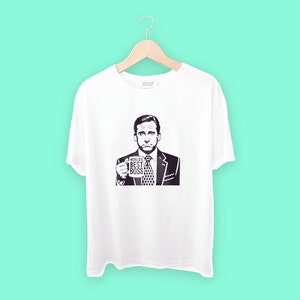 Puede incluir: Camiseta blanca con una imagen en blanco y negro de un hombre sosteniendo una taza que dice "World's Best Boss".