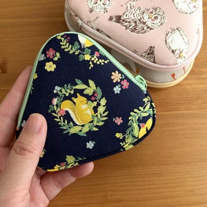 May include: A dark blue fabric pouch with a green zipper and a floral pattern featuring squirrels. The pouch is shaped like a triangle and has a light green trim.