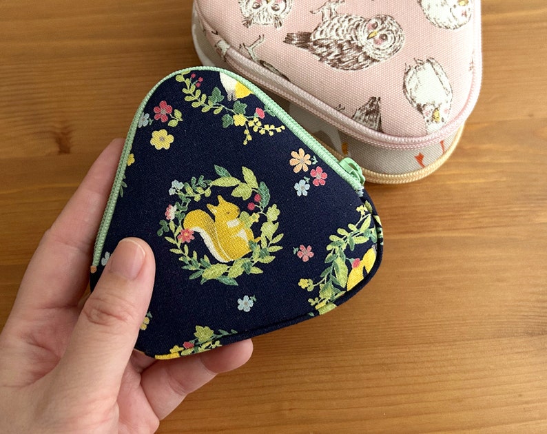 May include: A dark blue fabric pouch with a green zipper and a floral pattern featuring squirrels. The pouch is shaped like a triangle and has a light green trim.