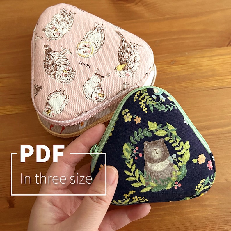 May include: Two fabric pouches in the shape of a triangle. The pouch on the left is pink with a white owl and bird pattern. The pouch on the right is dark blue with a green floral pattern and a brown bear in the center. The text "PDF In three size" is visible in the lower left corner of the image.