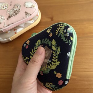 May include: A dark blue zippered pouch with a green zipper and a floral pattern. The pouch has a small bear illustration on it.