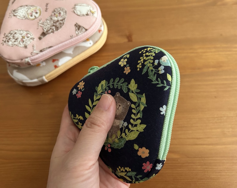 May include: A dark blue zippered pouch with a green zipper and a floral pattern. The pouch has a small bear illustration on it.