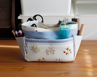 May include: A white fabric tote bag with a blue and white polka dot lining. The bag has multiple pockets and is filled with sewing supplies, including scissors, rulers, and pencils.