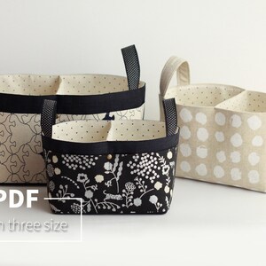 May include: Three fabric storage baskets with black trim and handles. The baskets are divided into two sections. The largest basket has a geometric pattern, the medium basket has a floral pattern, and the smallest basket has a polka dot pattern.  PDF In three size