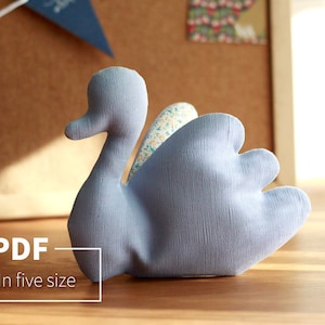 Puede incluir: Un cisne de tela azul claro con un ala con estampado floral. El cisne es un patrón de costura disponible en cinco tamaños. El texto "PDF - In five size" está impreso en un rectángulo blanco.