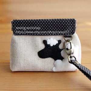 May include: A small, beige fabric coin purse with a black and white polka dot flap. The purse has a black and white cow applique and a white cloud applique. The purse has a black and white polka dot strap with a silver clasp.