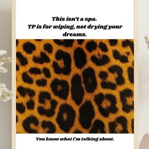 Puede incluir: Impresión artística enmarcada con un fondo de estampado de leopardo y el texto "This isn't a spa. TP is for wiping, not drying your dreams. You know what I'm talking about." El marco es de color beige claro.