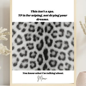 Puede incluir: Un estampado enmarcado con un borde color crema. El estampado presenta un fondo de estampado de leopardo y el texto: "This isn't a spa. TP is for wiping, not drying your dreams. You know what I'm talking about. Meow."