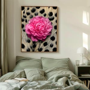 May include: A framed wall art piece featuring a large, vibrant pink peony flower. The flower is set against a background that mimics animal fur with black spots. The artwork is displayed above a bed with green bedding.