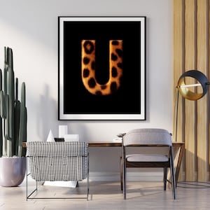 Könnte beinhalten: Gerahmtes Kunstwerk mit dem Buchstaben "U" in einem Leopardenmuster vor schwarzem Hintergrund. Das Kunstwerk wird in einem modernen Interieur mit Schreibtisch, Stuhl und dekorativen Elementen präsentiert.