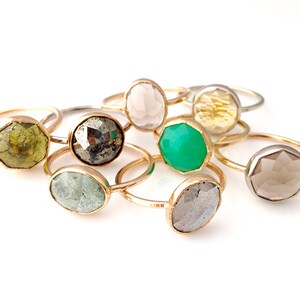 Op de afbeelding: Een verzameling van acht gouden ringen met verschillende gekleurde edelstenen. De edelstenen zijn bezel gezet en facetgeslepen. De ringen zijn allemaal van verschillende grootte en vorm.