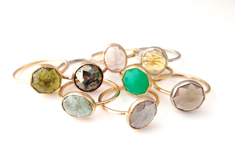 Op de afbeelding: Een verzameling van acht gouden ringen met verschillende gekleurde edelstenen. De edelstenen zijn bezel gezet en facetgeslepen. De ringen zijn allemaal van verschillende grootte en vorm.