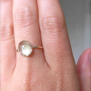 Op de afbeelding: Een gouden ring met een lichtgroene ovale edelsteen. De ring zit aan een vinger.